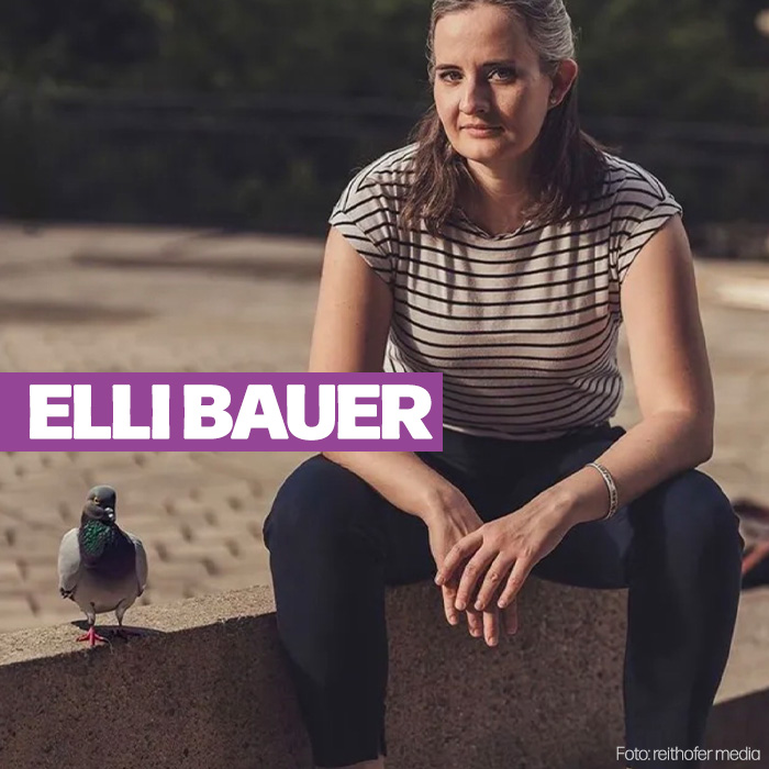 Kabarettistin Elli Bauer sitzt auf einem Steinsockel. Sie trägt Jeans und ein gestreiftes T-Shirt. Neben ihr auf dem Steinsockel sitzt eine Taube.