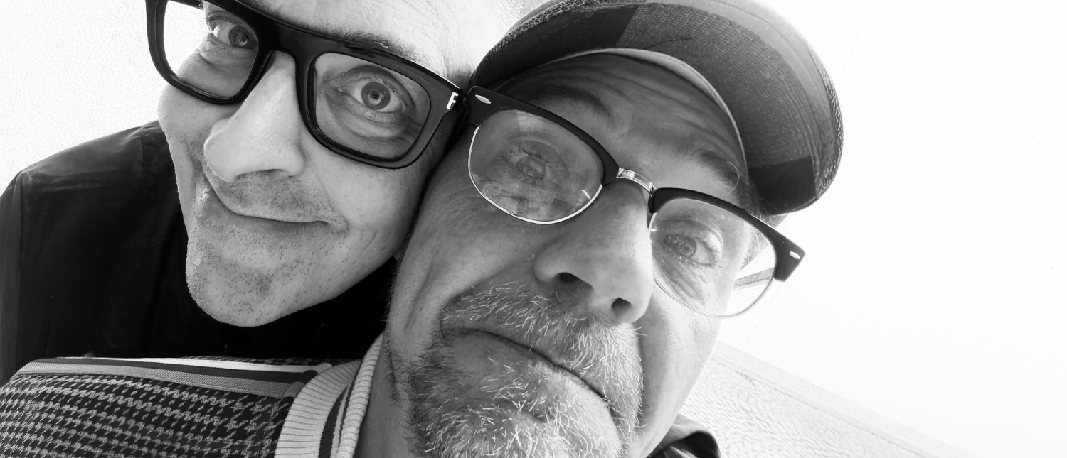 Schwarzweißfoto von Gebrüder Moped in Nahaufnahme. Franz Moped links und Martin Moped rechts sind eng aneinandergeschmiegt und füllen fast das gesamte Bild aus. Franz Moped grinst in die Kamera, Martin Moped schaut mit leicht entsetztem Gesichtsausdruck in die Kamera.